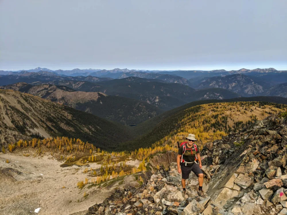 JR hiking up scree to ridge on Frosty Mountain Trail, with backdrop of mountains