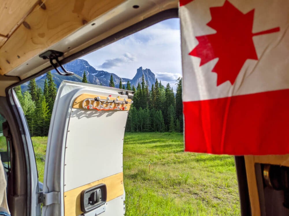 View out of side door of van conversion with mountains in background and Canadian flag in foreground