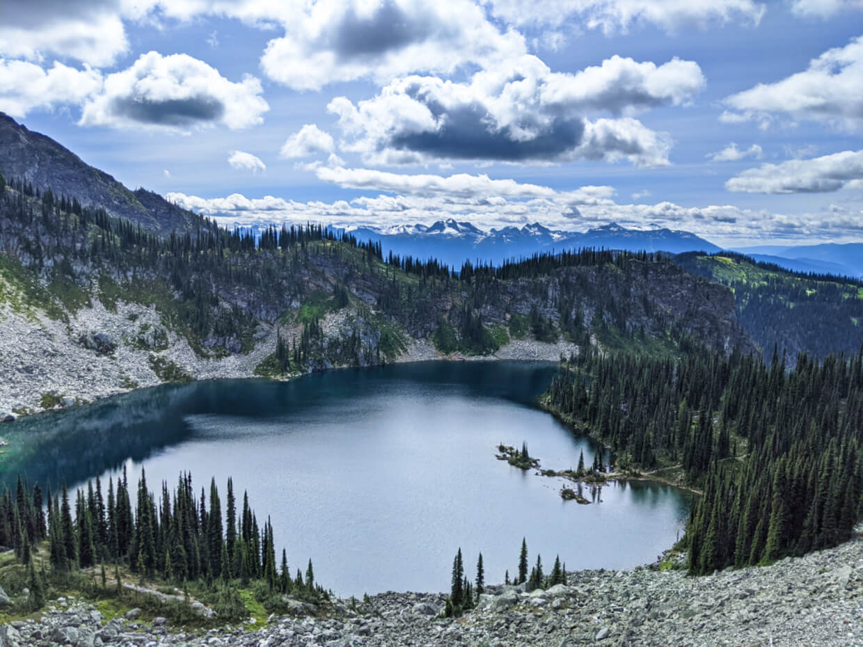 Looking down to a large deep blue lake from hiking trail, backdropped by mountains