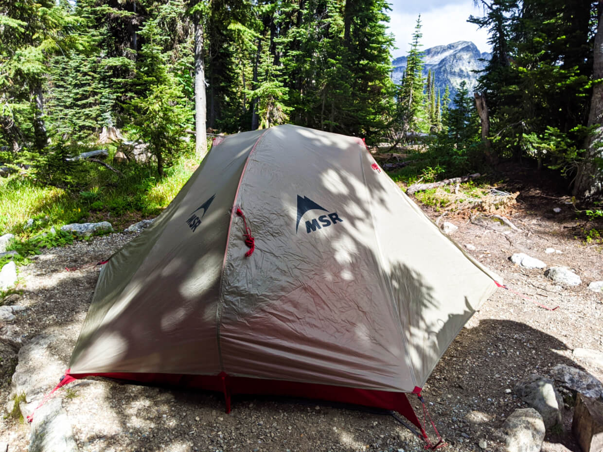 MSR tent set up on dirt tent pad near Eva Lake, with mountain peak in the background, seen through the trees
