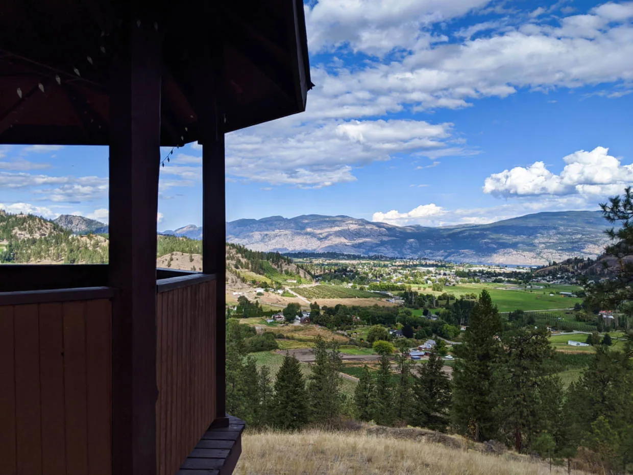 Side of wooden gazebo with views of the orchards and vineyards of Summerland below, with rolling mountains in the background