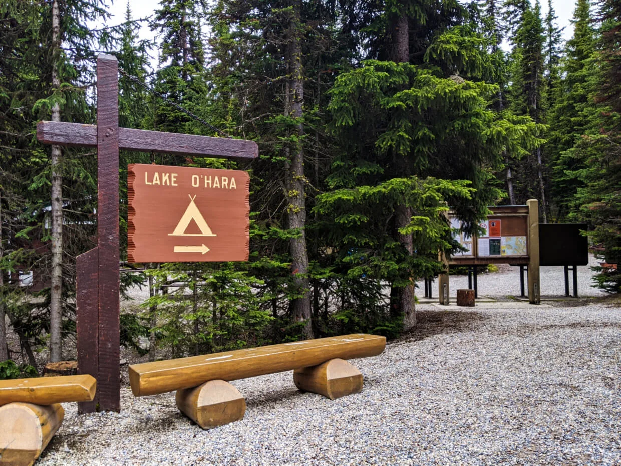 Wooden Lake O'Hara campground sign with benches signifying bus stop with campground entrance behind