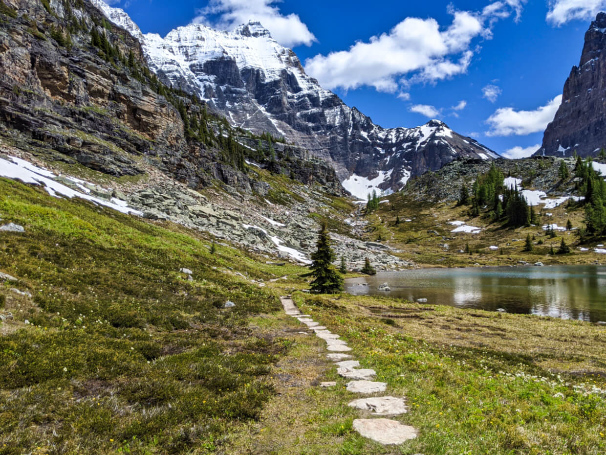 Looking back on a stone hiking trail towards lake surrounded by mountains