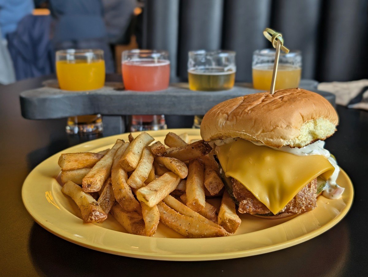 Close up of cheeseburger and fries at Yellow Dog brewing with colourful flight of beers in the background