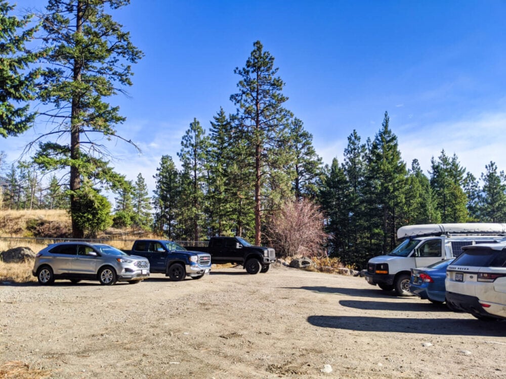 Pincushion Mountain parking lot with dirt surface, seven vehicles and background of pine trees