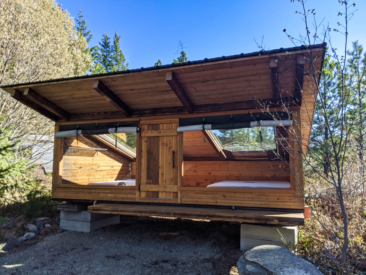 Looking towards a wide wooden hut with large windows and skylights, with two mattresses in side