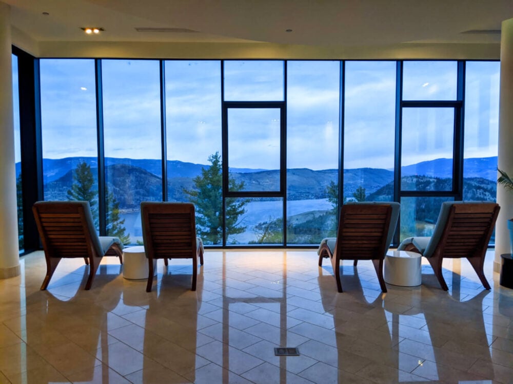 Four spa seats are lined up in front of floor to ceiling windows, looking out to Okanagan Valley scenery