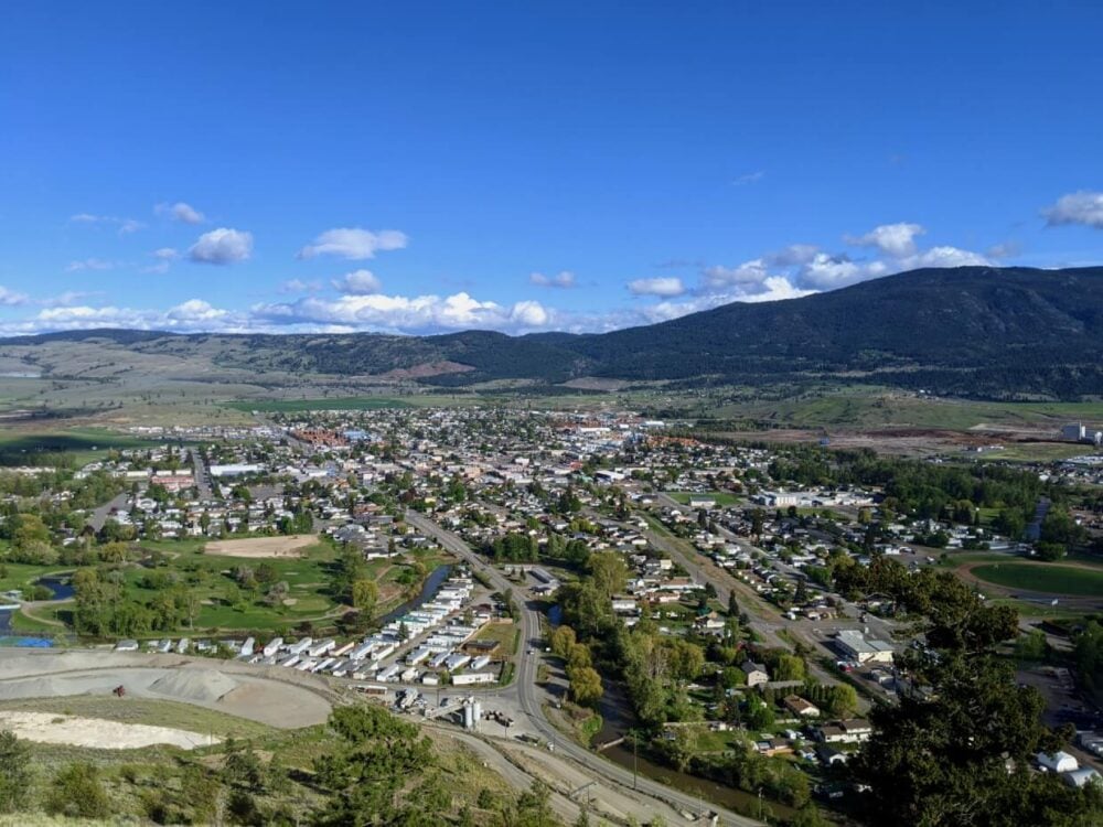 Elevated view looking down on the city of Merritt, with houses and highways leading away from camera, forested hills and mountains in background