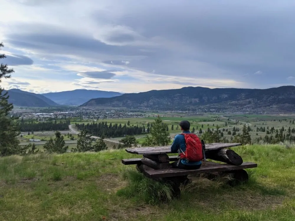 JR is sat with his back to camera, sat at a wooden picnic table looking out to views of Merritt and the Nicola Valley