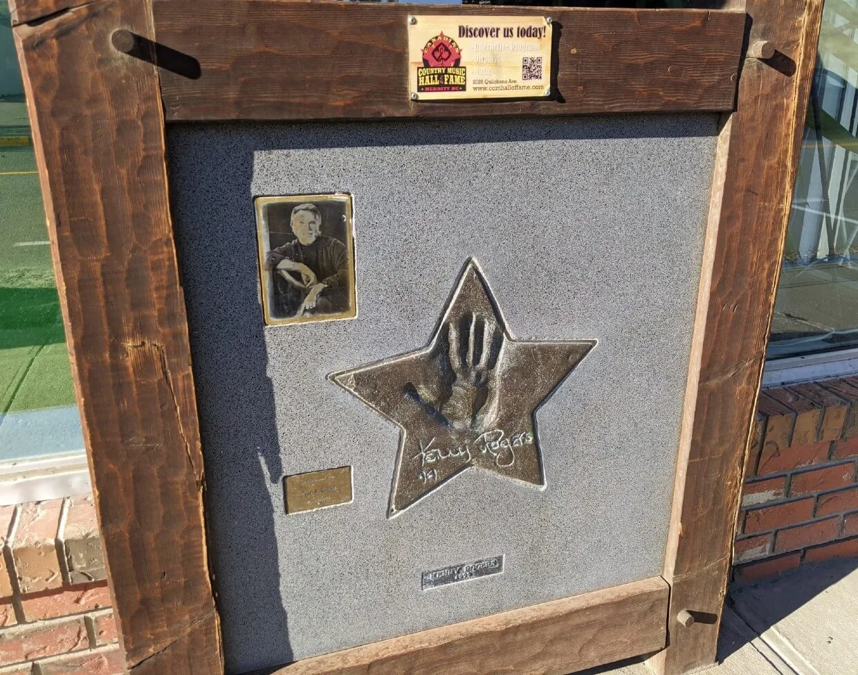  Close up of embossed gold star with Kenny Rogers hand print and signature on wooden plaque, with photograph of musician on left