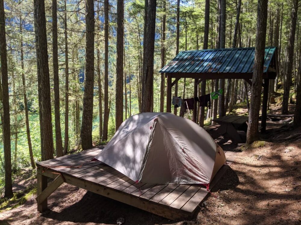 Set up tent on wooden tent pad in forest next to Spectrum Lake in Monashee Provincial Park. There is a wooden shelter to the right
