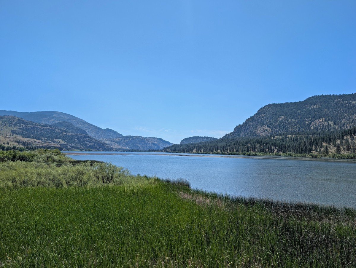 View of Vaseux Lake from boardwalk, with layers of forested hills and marshland in foreground