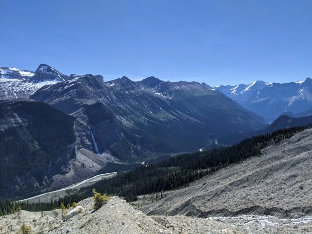 Looking across glacier moraine towards mountains and glaciers on other side of valley, with large cascading waterfall (Takakkaw Falls) on left hand side