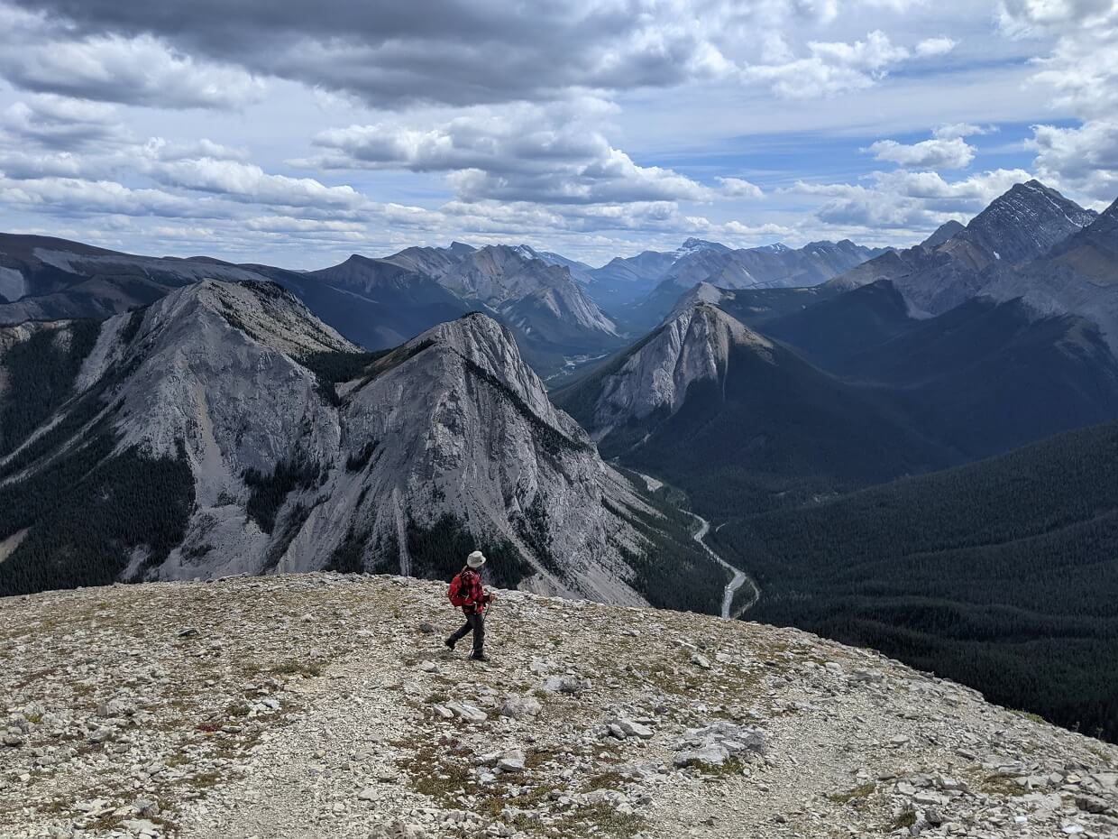 Side view of JR hiking on mountain top, looking over at other mountain peaks below