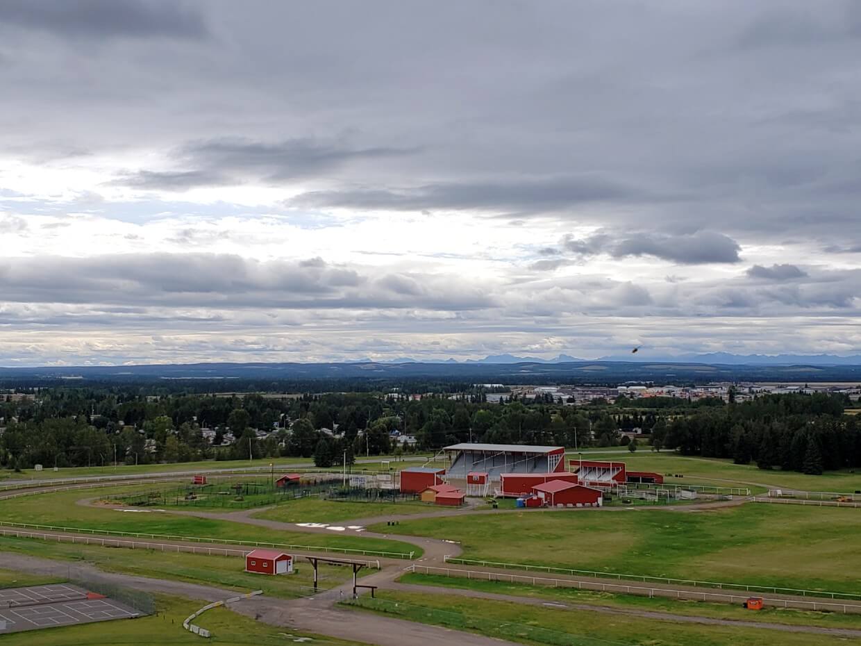 Viewpoint panorama of Sundre and surrounding scenery, including red rodeo grounds in foreground and rocky mountains in background