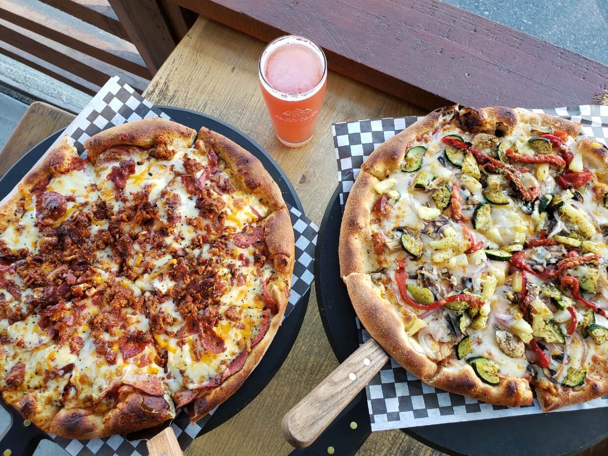 Overhead view of two pizzas and a beer at Mount Arrowsmith Brewing Company