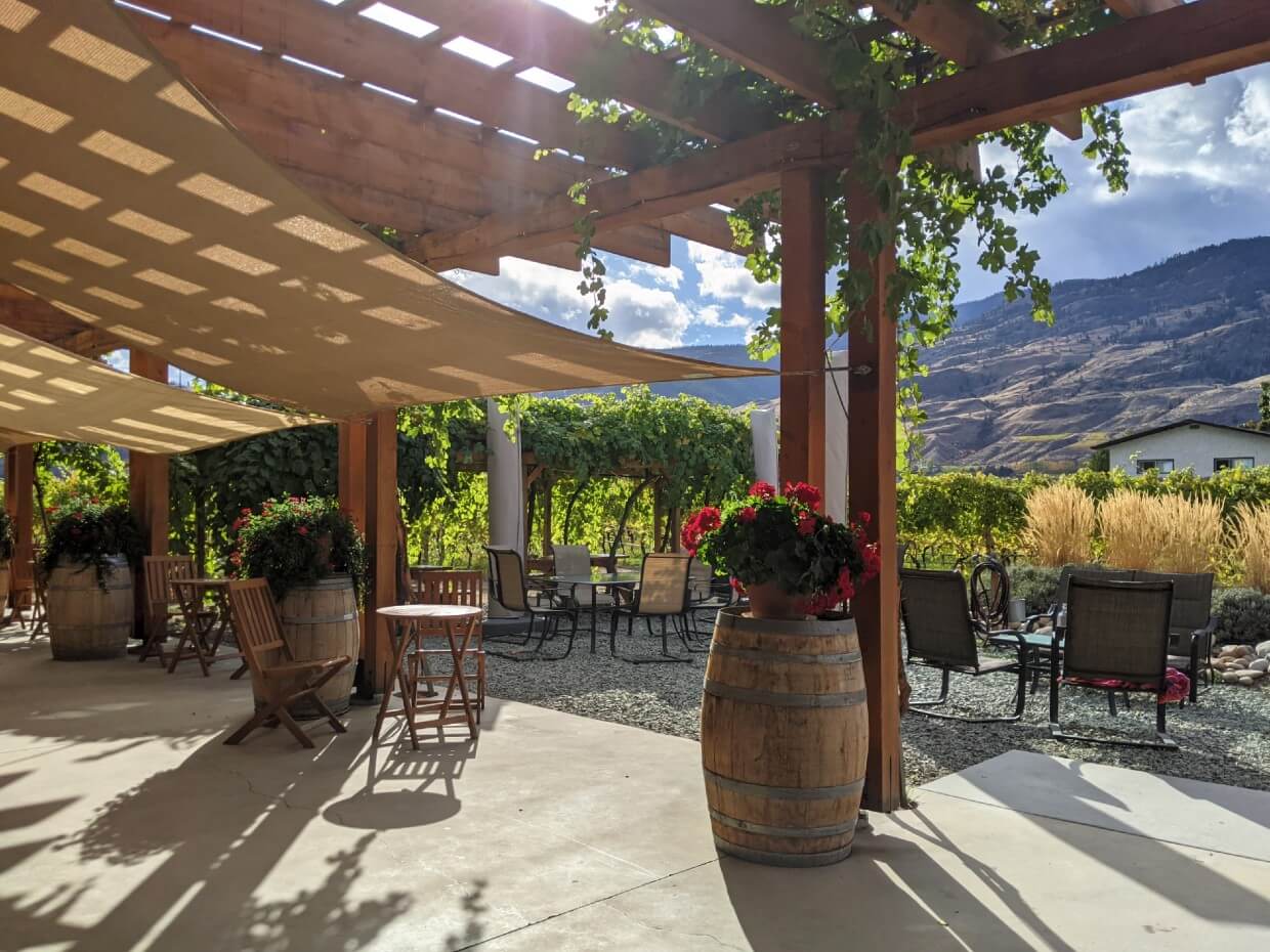 Tasting bar view of Bartier Bros. patio, with seating under shade and vineyards beyond