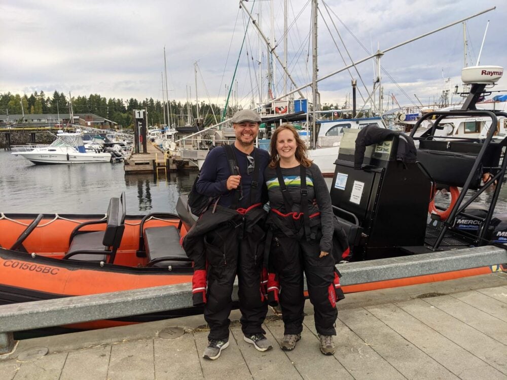 Front view of JR and Gemma in front of whale watching zodiac boat in Parksville. Both are wearing floatation suits