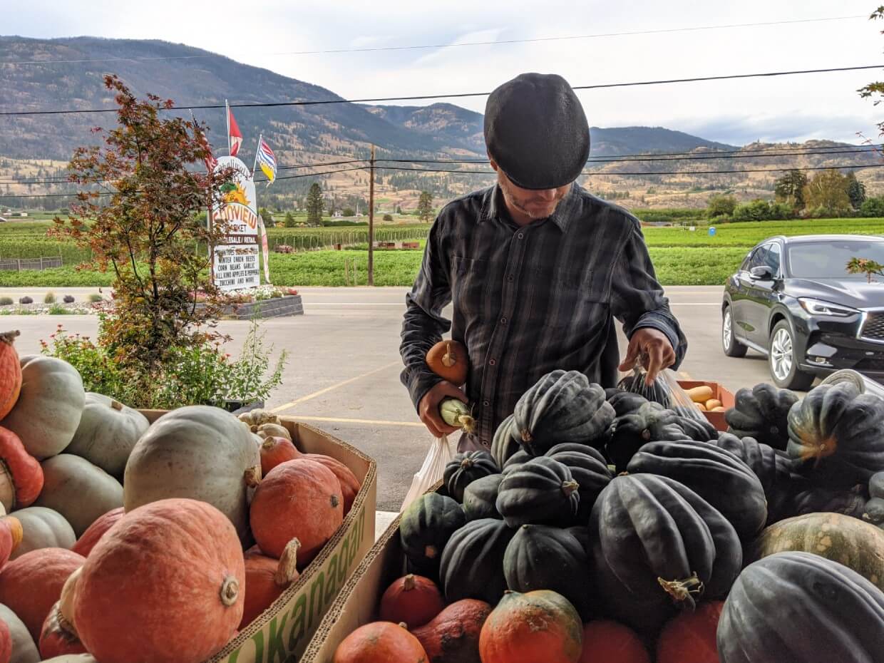 Looking across bins of squash and pumpkins to JR choosing squash to buy 