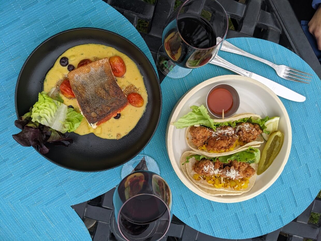 Overhead view of two plates and two glasses of wine at Nk'Mip Cellars, with one salmon dish and one chicken taco dish