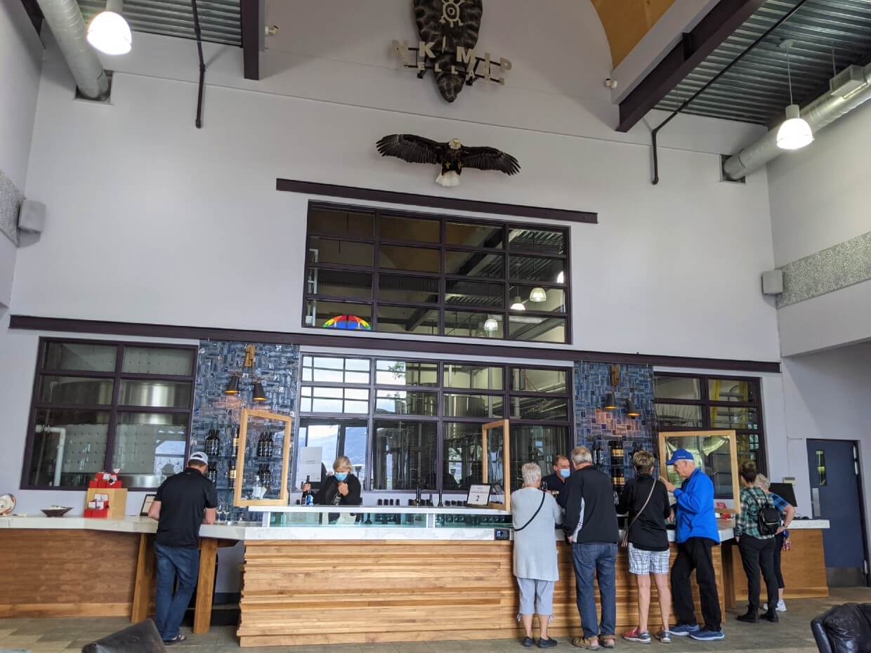 View of Nk'Mip Cellars tasting room with tasting bar, high ceilings, Bald Eagle model, winery logo and wine tasters sipping 