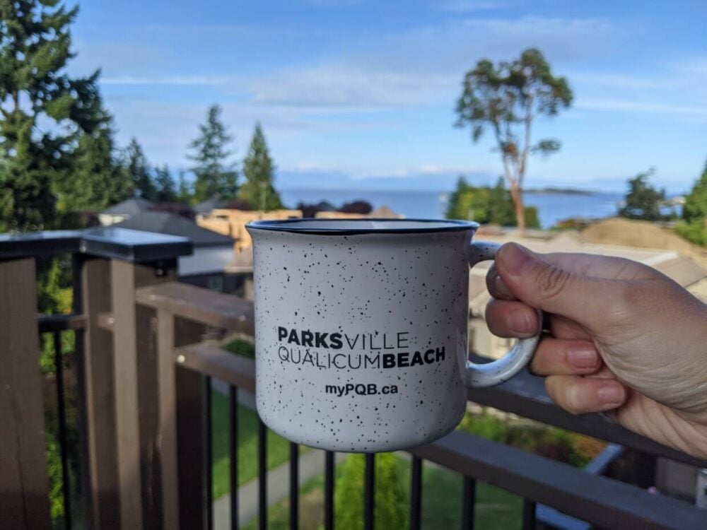 Close up of white Parksville Qualicum Beach mug in front of sunny ocean view at Sunrise Ridge Waterfront Resort