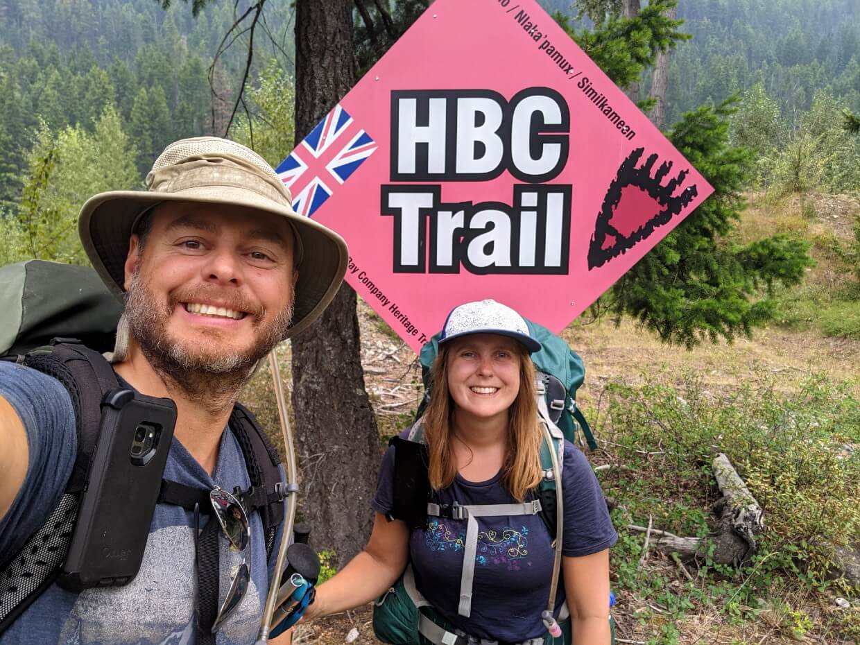 Selfie of JR and Gemma finishing the HBC Trail, with large red diamond shaped HBC Trail sign in background