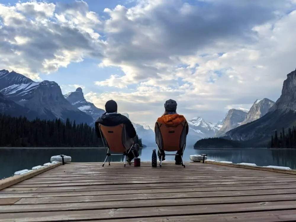 Back view of Gemma and JR sat in chairs on boat dock at Spirit Island, with mountains in background