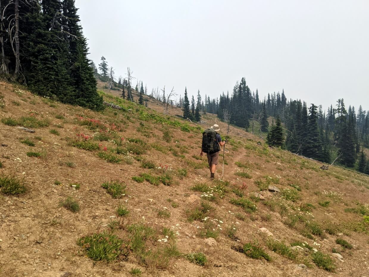 Back view of JR approaching Olivine Campground on narrow dirt trail on mountain slope