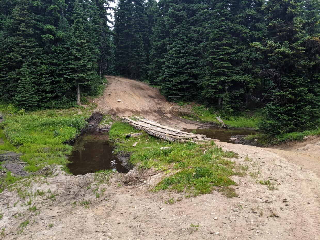 Looking across wooden bridge and mud to 4X4 dirt track