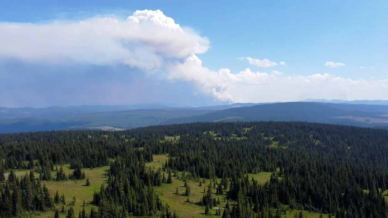 Drone photo of wildfire in distance, behind forested plateau