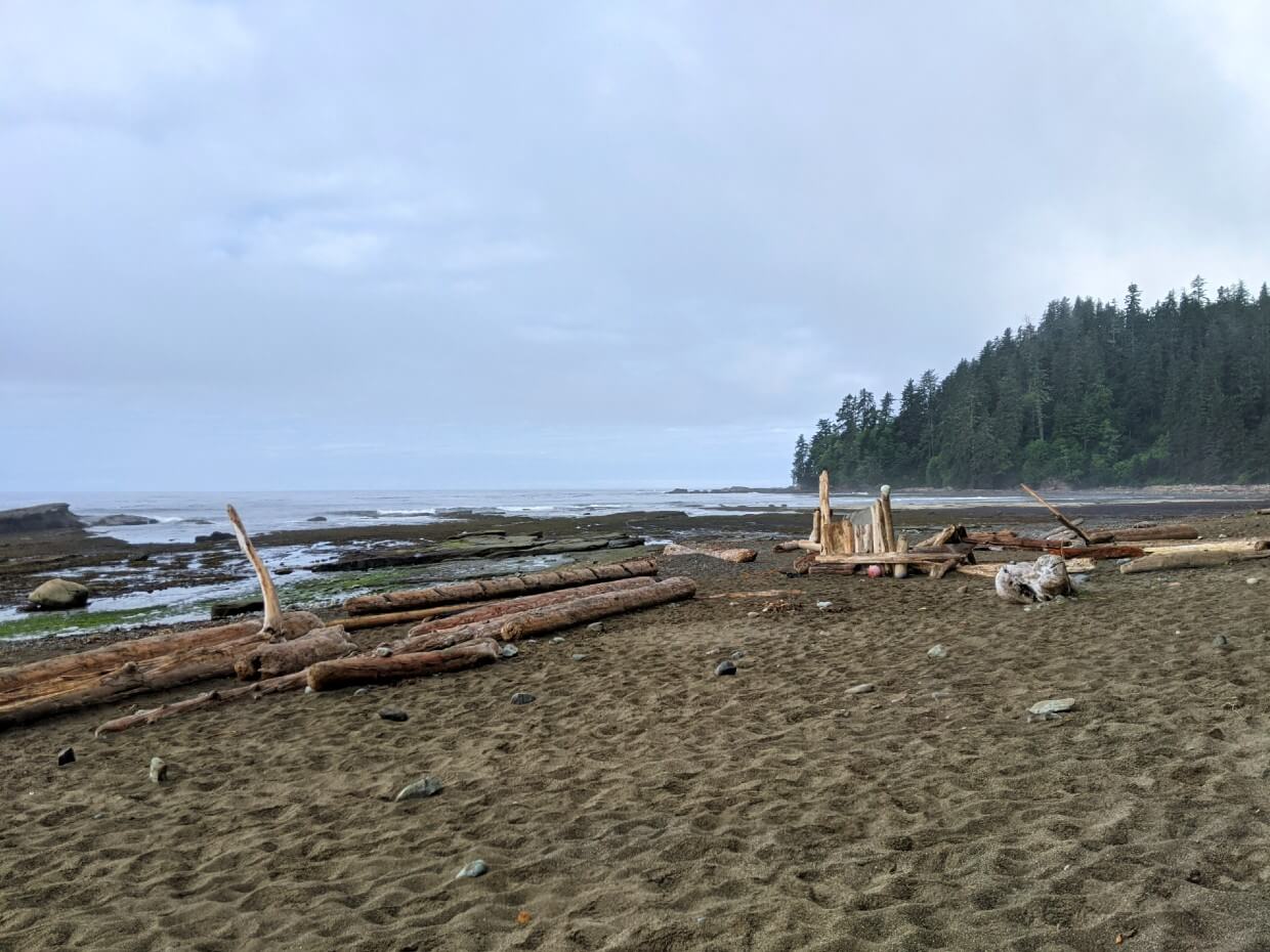 View of Michigan River campground on the West Coast Trail - sandy beach and driftwood in front of calm ocean