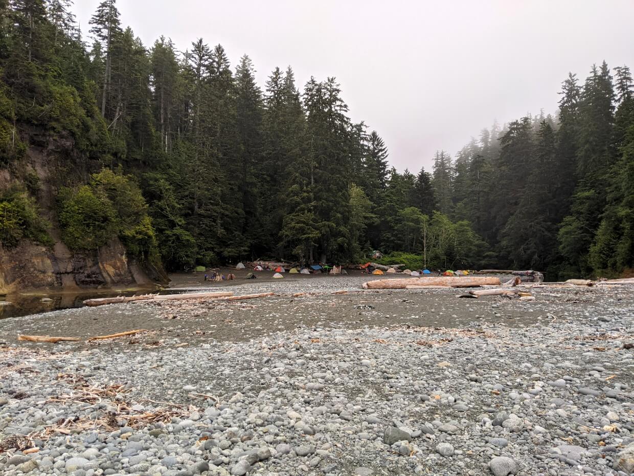 Looking towards Camper Bay campground, where there are over a dozen colourful tents set up by the treeline, at the edge of the beach