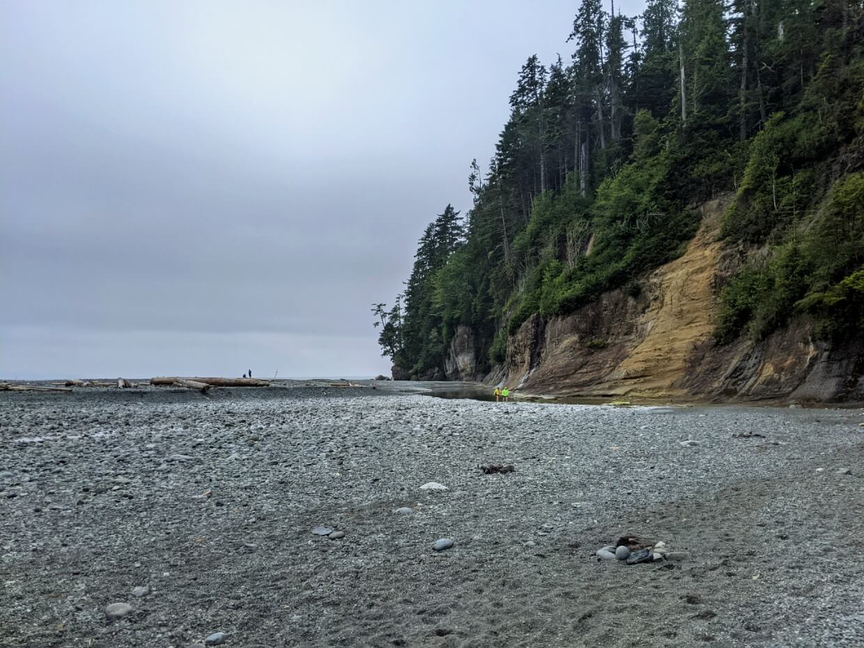 Looking across grey pebble beach at Camper Bay Beach towards tall headland