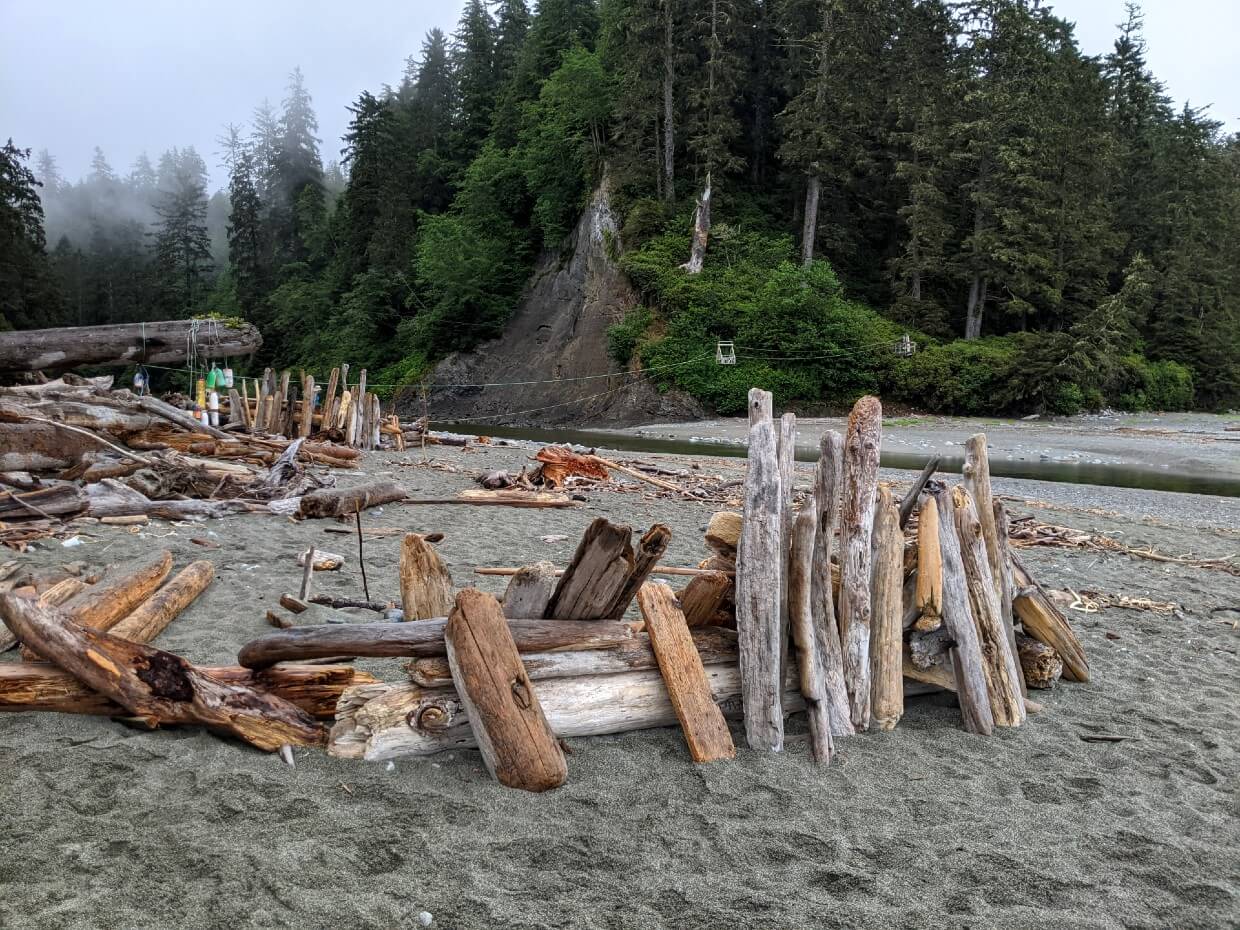 Driftwood structures on sandy Carmanah Beach on the West Coast Trail, backdropped by forest