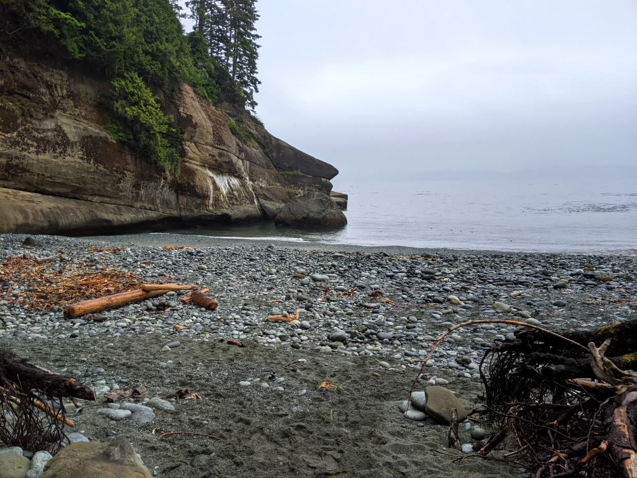 Looking out from camping area towards grey pebble beach and tall headland