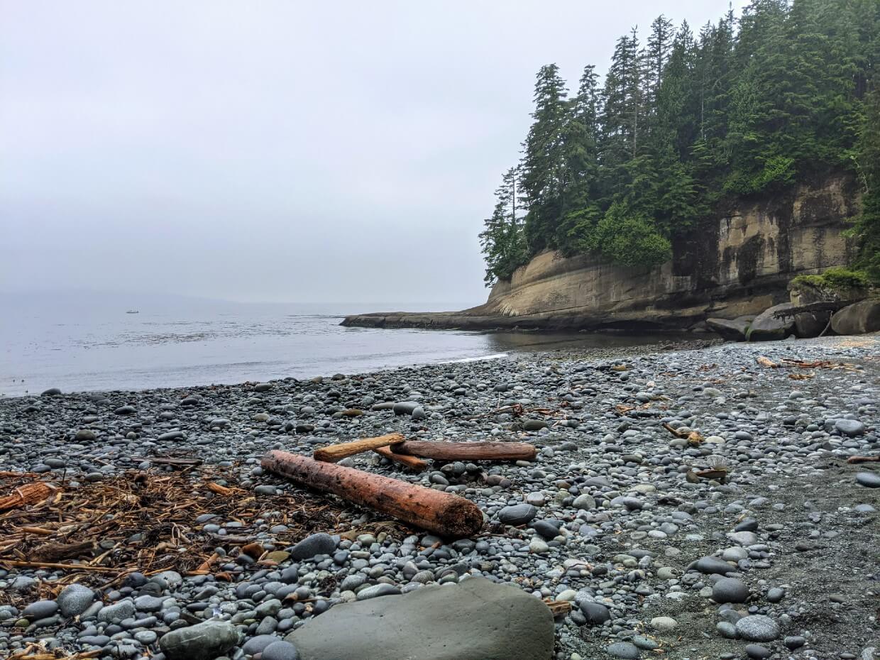 Grey pebble ocean beach with tall forested headland at Cullite Cove on the West Coast Trail