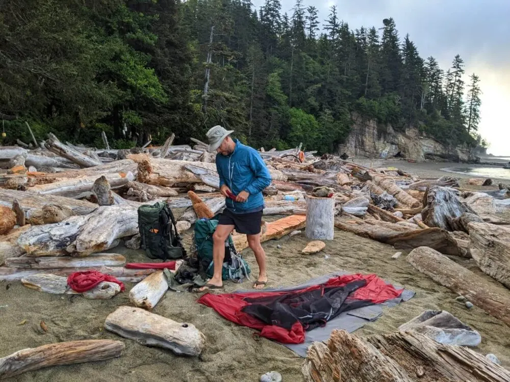 JR standing next to collapsed tent on sandy beach on the West Coast Trail, surrounded by driftwood