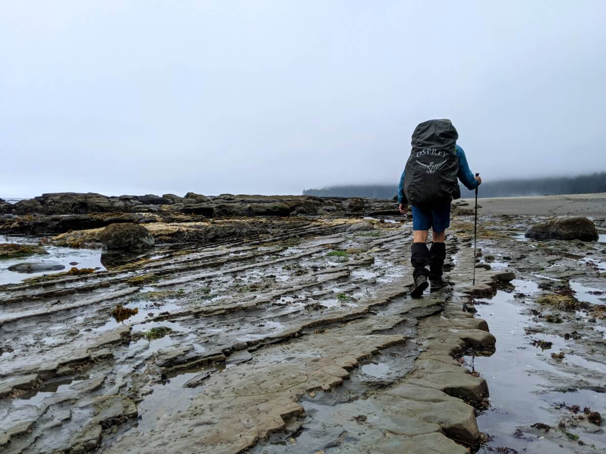 Back view of JR hiking on rocky shelf surface on West Coast Trail - he is holding a hiking pole in his right hand