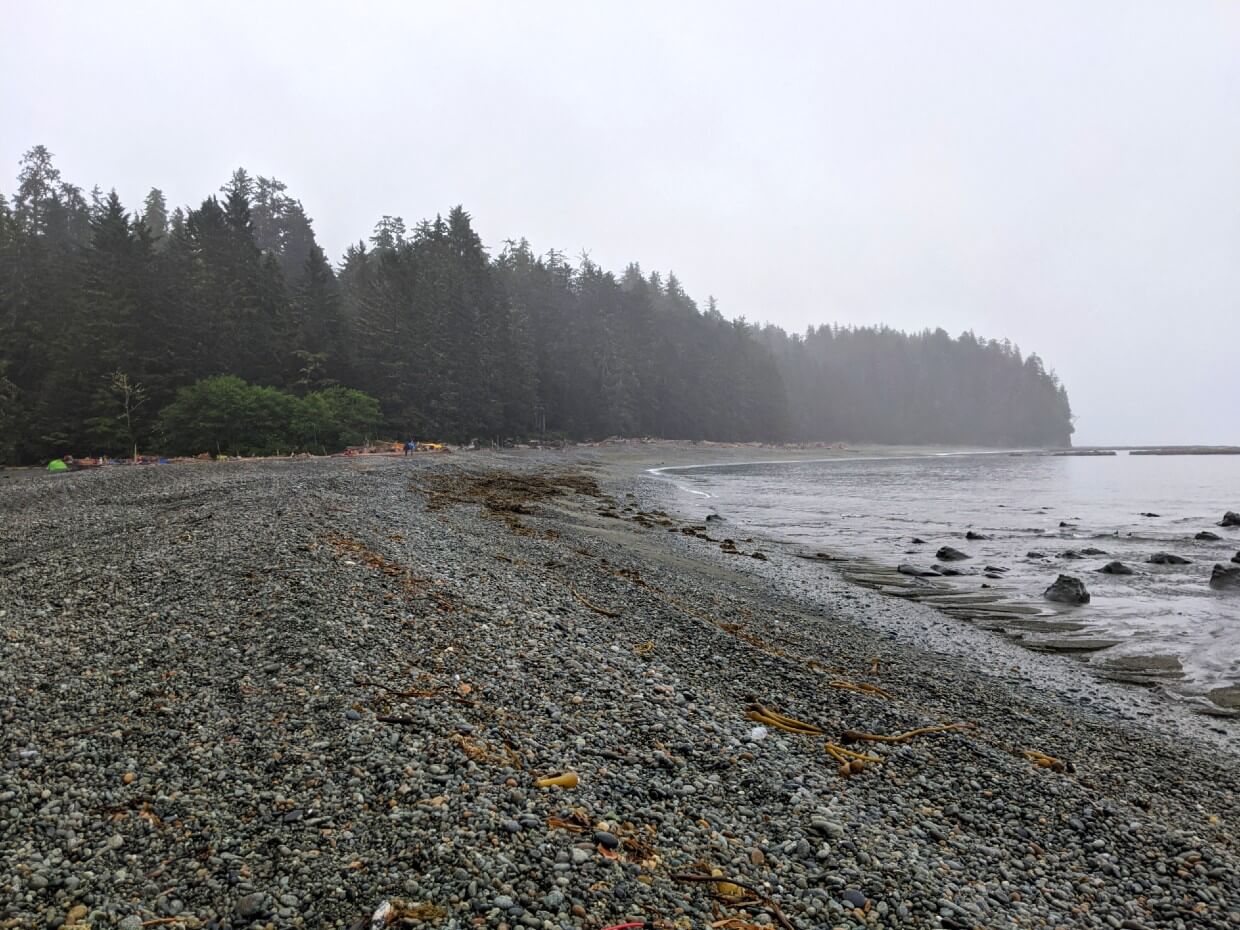 Looking across grey pebble beach at Walbran Creek - there are colourful tents visible in the background
