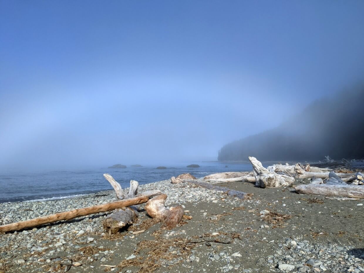 Sand and pebble beach next to ocean in morning, with white rainbow