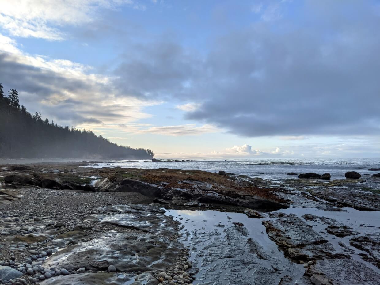 Coastal view with rocky beach and headland in distance, with blue skies and clouds