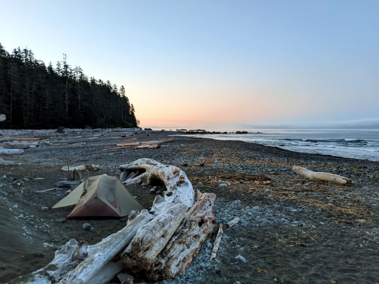 Sunrise on Klanawa Beach, with set up tent next to driftwood and beach stretching across background