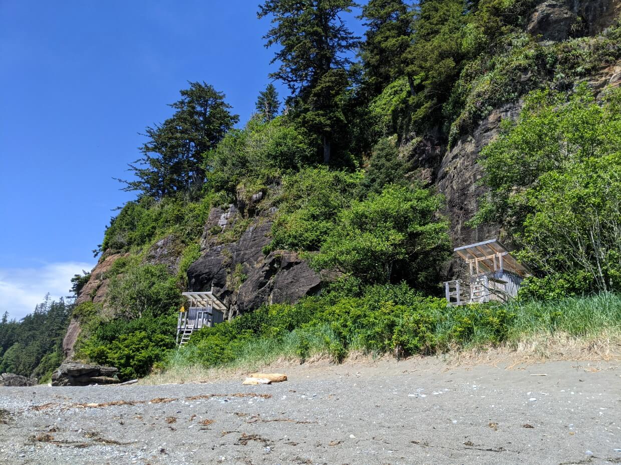 Two elevated wooden composting outhouses sit beneath cliffs at Tsusiat Falls Camp