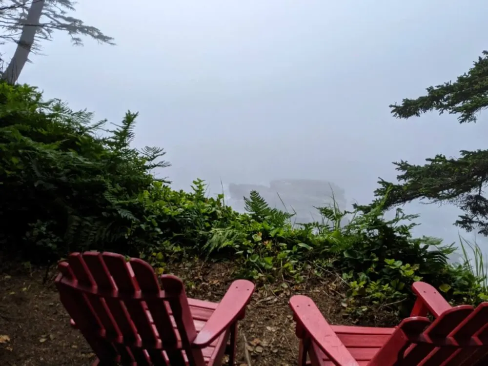 Two red Parks Canada chairs sit in front of a misty bluff view