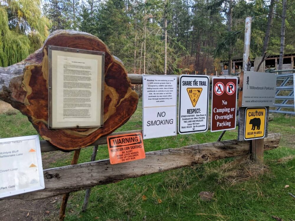 Wooden fence with trail signage at Willowbrook trailhead, including no camping signs, bear aware sign, trail market information and more