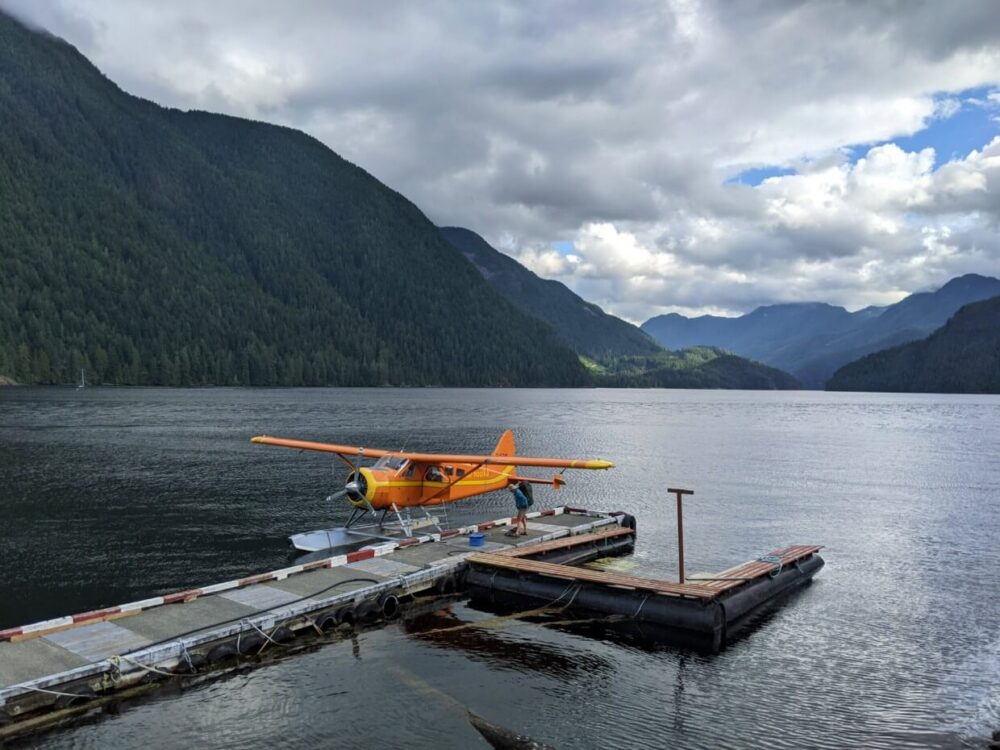 Orange seaplane parked and floating next to dock at Gold River, with ocean and mountains visible beyond