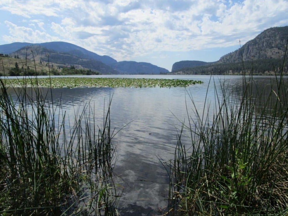 Looking across calm lake surface towards vertical rock face formation on other side of lake