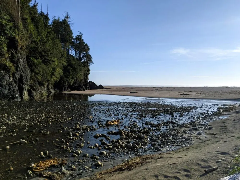Wide and rocky creek outlet at First Beach, with sandy beach beyond