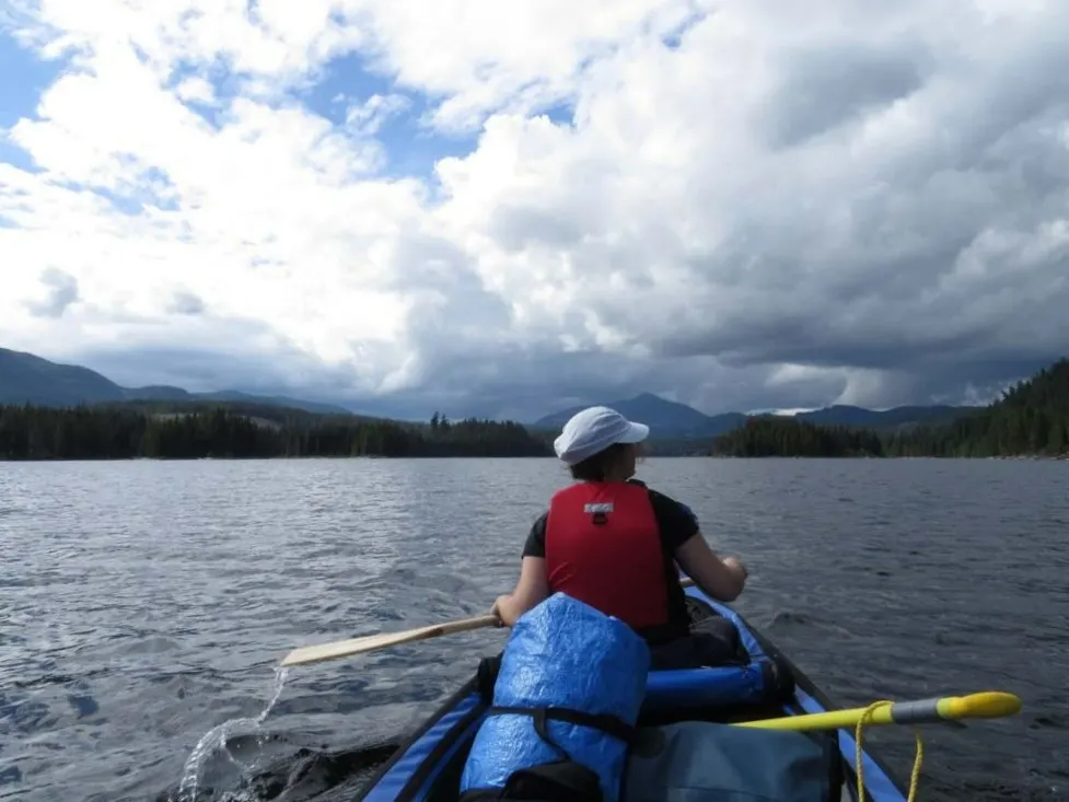 Back view of Gemma paddling a canoe on Horseshoe Lake with forest and low mountains in background